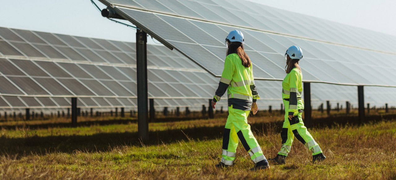To ansatte i verneutstyr ved siden av et solcelleanlegg