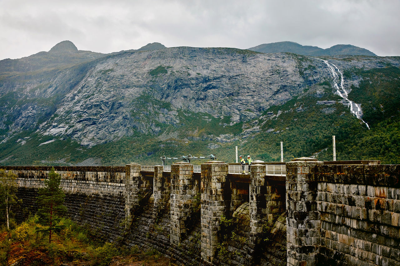 To mennesker står på en demning med fjell i bakgrunnen