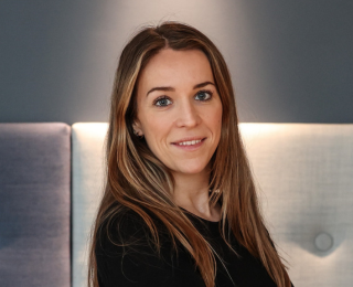 Dame med brunt hår og armene i kors smiler